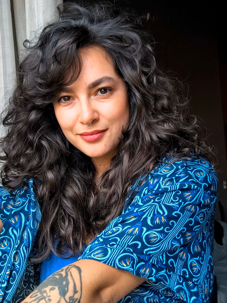 Foto de Pamela Oliveira com blusa azul. É uma educadora feminista, jornalista, comunicadora popular e também socióloga.